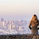 Woman Sitting on Rock Wall, Looking at City