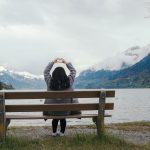 Woman Sitting on Bench at Lake Holding Hands in the Shape of a Heart